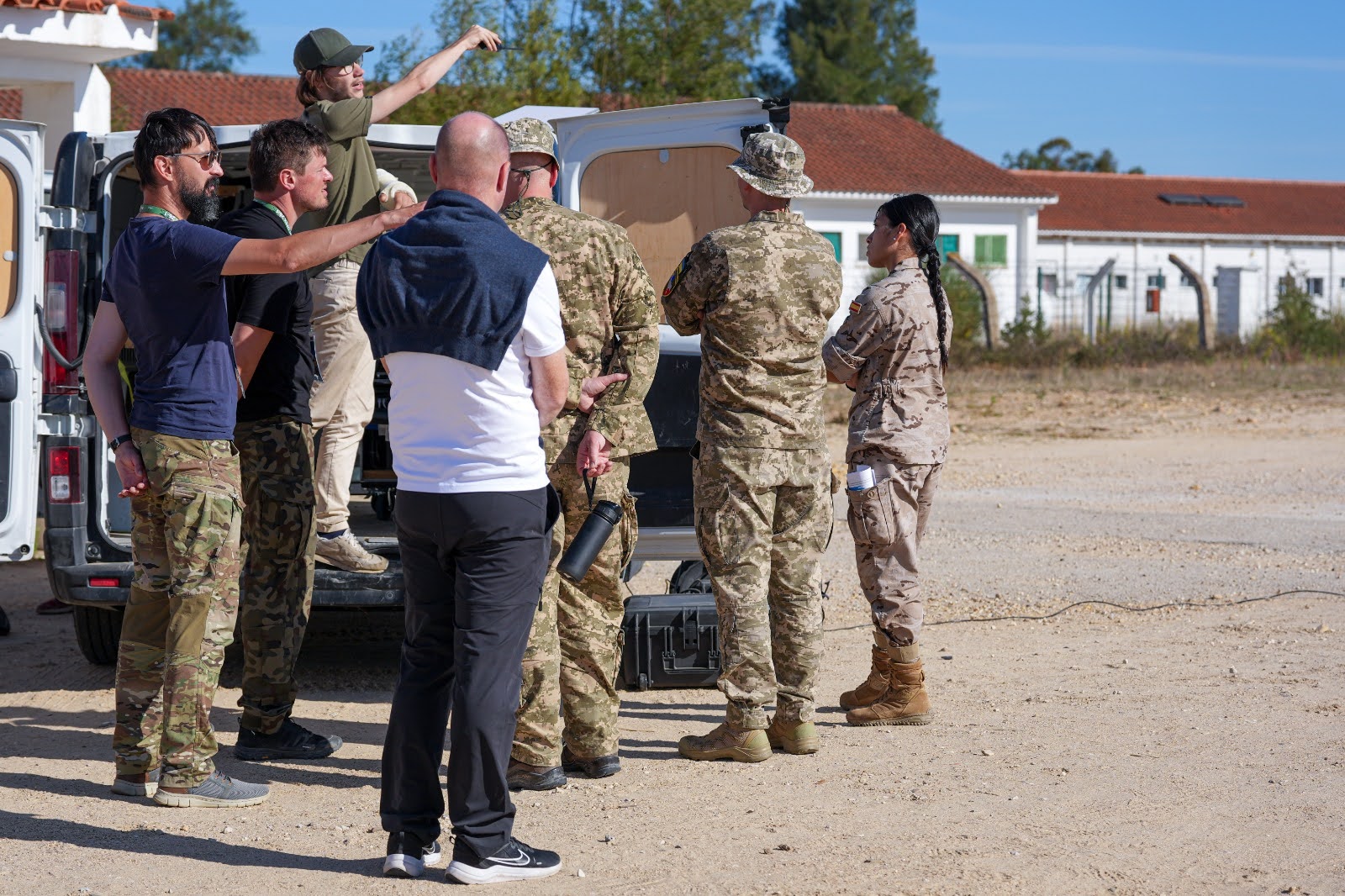 Military personnel and technicians gathered around the open back of a van during field trials.